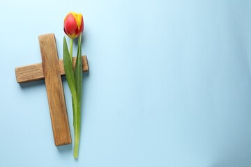 Easter - celebration of Jesus resurrection. Wooden cross and tulip on light blue background, top...