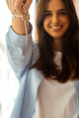 Obraz premium Happy woman holding keys to new home, looking at camera and smiling. Portrait of first time buyer, house owner, apartment renter, flat tenant or landlady. Moving day and buying own property concept