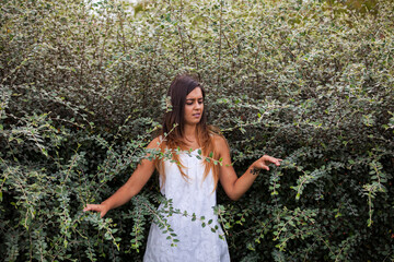 beautiful woman in a white dress, gracefully posed amidst lush green vegetation - 750972370