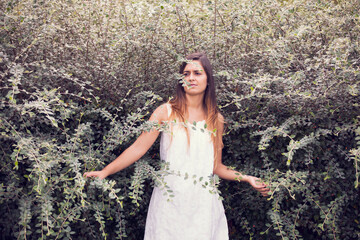 beautiful woman in a white dress, gracefully posed amidst lush green vegetation - 750972392