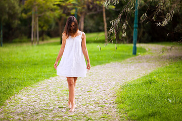 beautiful woman in a white dress, gracefully walking barefoot on a cobblestone path in a serene park - 750972393