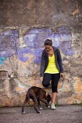 young woman playfully interacting with a Boxer dog, against a graffiti-covered wall in an urban setting. - 750972518