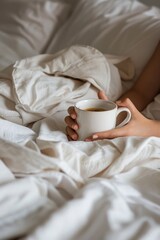 A person holding a cup of coffee on a bed. Suitable for lifestyle or morning routine concepts
