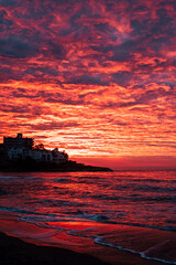 Red sunset at the beach with town in silhouette and dramatic sky with clouds. Amazing sunlight...