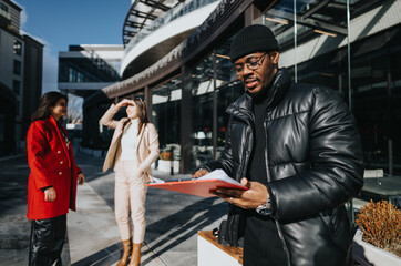 Three diverse colleagues engage in a casual business discussion outside a modern office building, with one holding a clipboard.