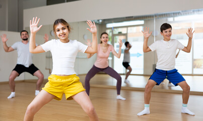 Fototapeta na wymiar Cheerful girl exercising in family group during dance class at dance studio