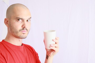 expressive bald man in red tshirt , drinking in a white cup