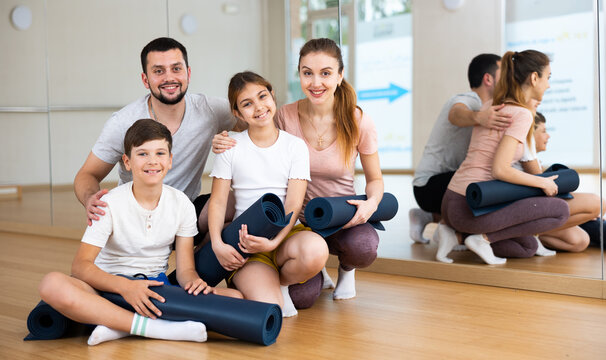 Group photo of positive family with rolled mats in fitness studio.