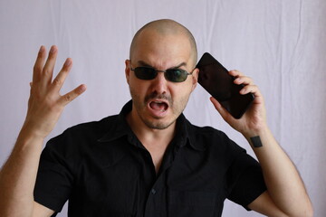 expressive bald man with black shirt and sunglasses  interacting with his smartphone 