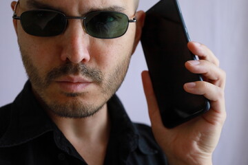 expressive bald man with black shirt and sunglasses  interacting with his smartphone 