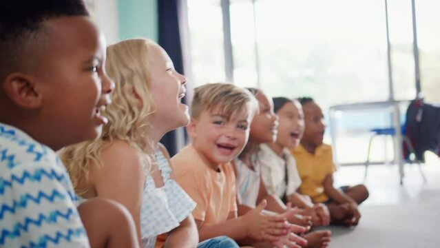 Line of laughing primary or elementary school students sitting on floor during classroom lesson - shot in slow motion