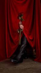 Rosas rojas entre manos con fondo de tela roja, con uñas color rojo sostienen rosas rojas en un...