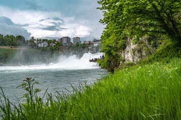 Tourists enjoy the powerful water floods of the mighty Rhine Falls from the viewing platform. Rhine...