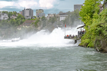 Tourists experience the powerful water floods of the mighty Rhine Falls from the viewing platforms....