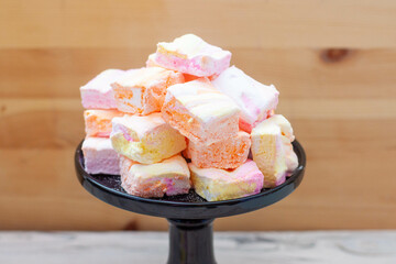 Colorful pink, orange and yellow homemade marshmallows made of egg whites and sugar on a black cake stand