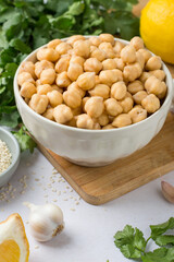 Chickpeas in a bowl, lemon, olive oil, sesame, cilantro, garlic on a wooden board, on a light background. The process of making hummus. Eastern cuisine.