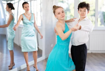 Cercles muraux École de danse Enthusiastic teenagers, boy and girl in formal wear performing elegant waltz in pair in sunny hall of dance school during lesson with female instructor..