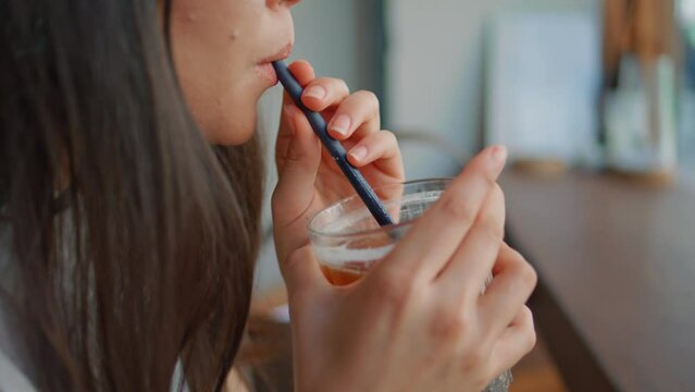 Unrecognizable girl drinking cocktail from straw in modern urban bar close up. 