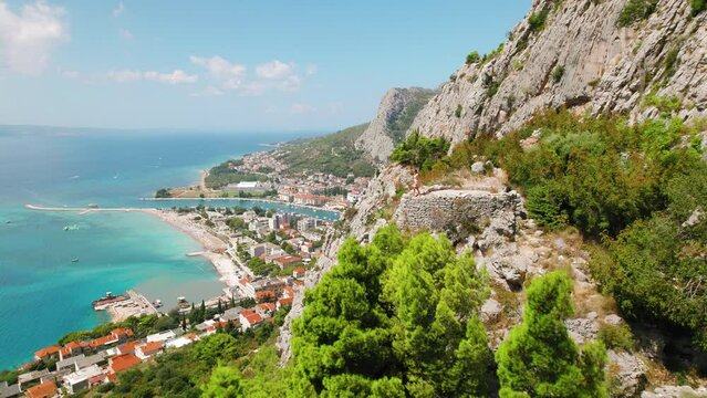 Aerial view of a sunlit Omis town by the emerald sea and rocky terrain. Summer Croatia from above.