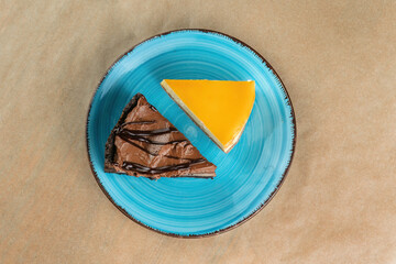 A slice of orange cheesecake and a slice of chocolate cheesecake on a blue plate.
