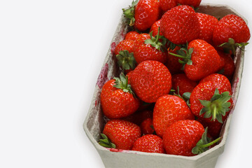 Freshly harvested ripe garden strawberries in recycled paper food container on a white background, top view close-up. Copy space.