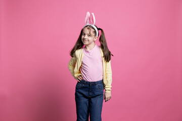 Little girl feeling happy and dancing in front of the camera, fooling around and acting silly against pink background. Young toddler wearing bunny ears and posing with confidence in studio.