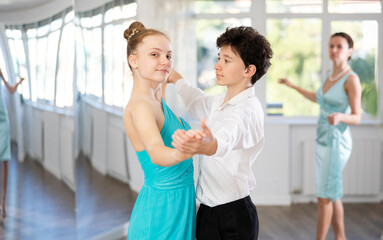 Girl and a boy in festive clothes learn to dance tango under guidance of a teacher