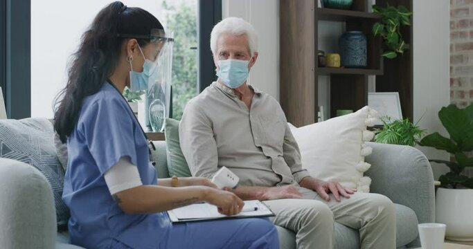 Thermometer, clipboard and caregiver check old man for fever virus, cold disease and health problem in retirement home. Mask, patient assessment and nurse writing test results of temperature reading