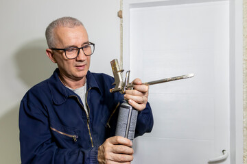 A mature man installing a door frame of an interior door with a polyurethane foam gun. The use of...