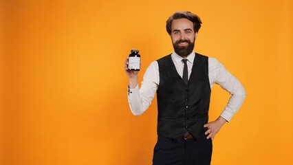 While working as waiter, fine dining staff displays bottle of healthcare vitamins while holding...