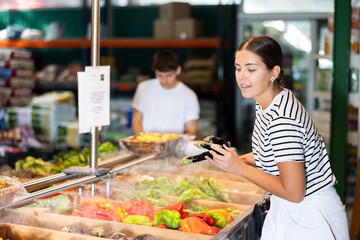 Fototapeta na wymiar Young woman shopper choosing eggplants in grocery store