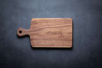 Handmade wooden cutting board background. A handcrafted black walnut wood chopping board sits on a dark-toned tabletop. walnut wood board. 