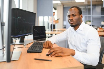 African American trader works at computer with displayed real-time stocks