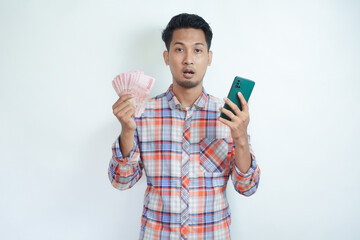 Adult Asian man showing confused face expression when holding mobile phone and paper money