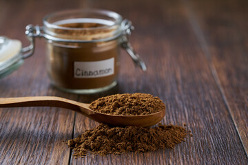 cinnamon powder poured out of a wooden spoon on a dark wooden table, selective focus.