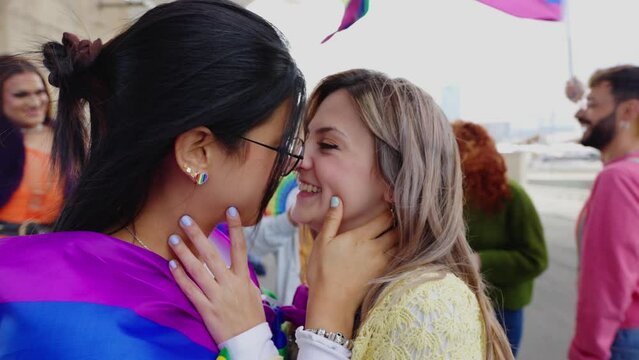 Young female couple in love kissing during gay pride parade festival day. LGTB community people having fun celebrating together outdoors