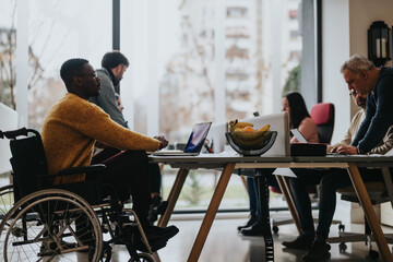 Inclusive work culture depicted with multi-ethnic team including a person with a disability engaging in a collaborative work session in a bright office.