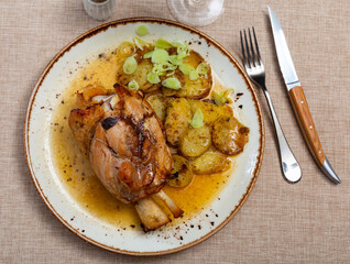 Appetizing pork knuckle baked in oven with boiled potatoes in white plate