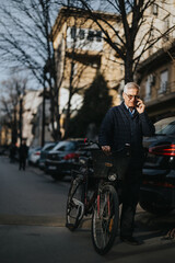 Naklejka premium An elderly man talks on a mobile phone, leaning on a bicycle with buildings in soft focus in the background, illustrating urban life and connectivity.