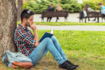 Obraz premium College student with book. Student guy doing homework in the park.