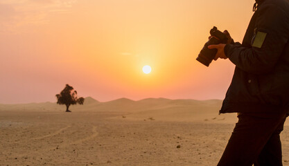 silhouette of a person with a camera in the desert against the backdrop of sunrise. dawn in the desert with a person with a camera in his hands in the foreground - 751032928
