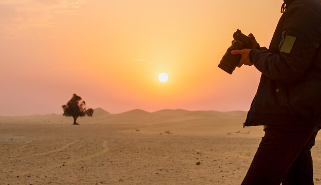 silhouette of a person with a camera in the desert against the backdrop of sunrise. dawn in the desert with a person with a camera in his hands in the foreground