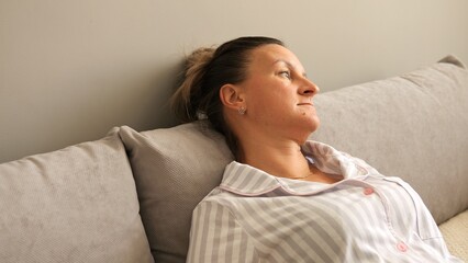 Tired woman lies on sofa, staring into space. Fatigue evident in her eyes and posture. She embodies...