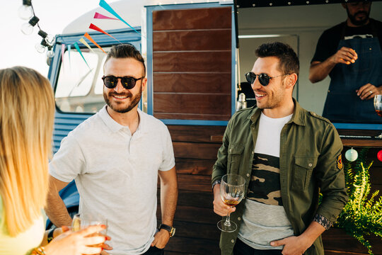 Hispanic friends chatting and drinking wine near truck