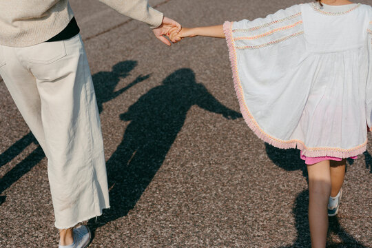 Anonymous Mother and daughter hand in hand walking on asphalt