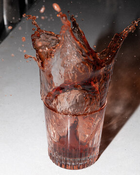 Ice cube dropping into a cup of red liquid.