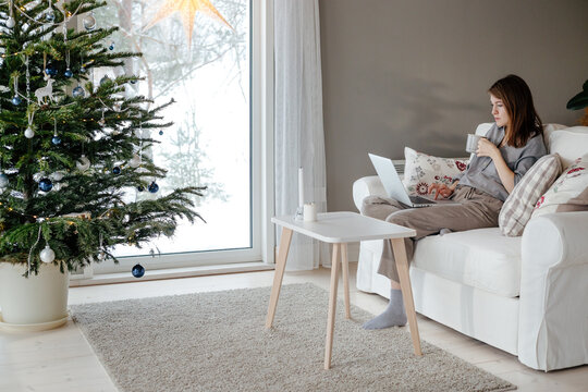 Woman drinking tea while using laptop at Christmas holiday