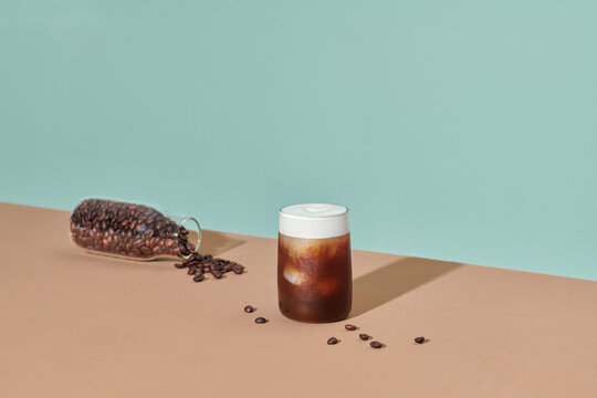 Ice coffee in a glass with cream poured over and coffee beans.