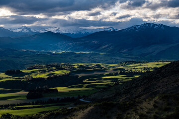 Aerial view of green meadows and mountains lit up by dappled light