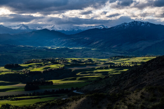Aerial view of green meadows and mountains lit up by dappled light
